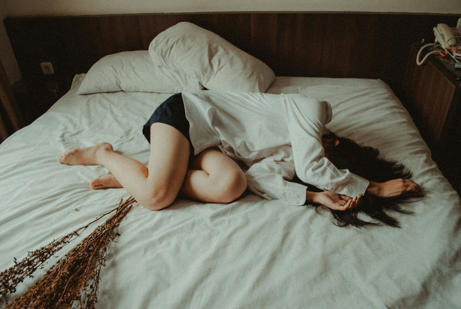 A woman is lying in bed in pain. Credit: Yuris Alhumaydy @ Unsplash