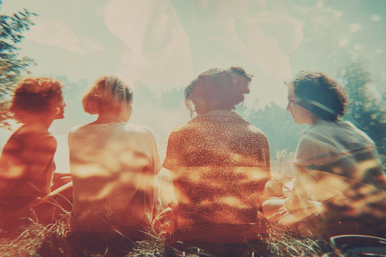 Four people sitting together in a natural setting with a warm, blurred effect.